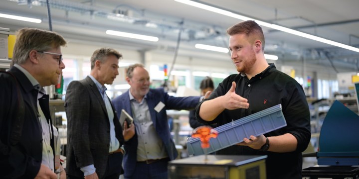 Mitarbeiter zeigt interessierten Zuschauern Produkte in blauer Box