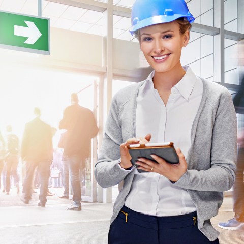 Femme souriante avec un casque de sécurité et une tablette à la main lors de l'évacuation d'un bâtiment