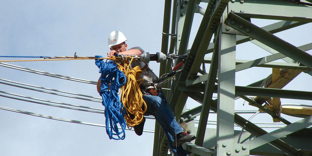 Arbeiter mit Schutzhelm führt Wartungsarbeiten an einem Strommast durch
