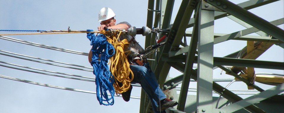 Travailleur avec casque de protection effectuant des travaux de maintenance sur un pylône électrique