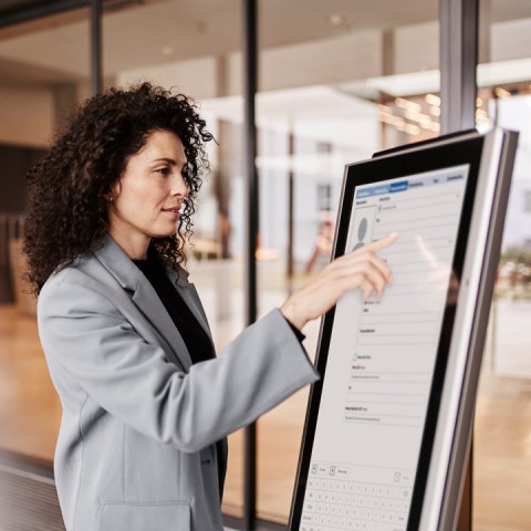 Frau im Eingangsbereich eines Gebäudes am digitalen Selbstanmeldungs-Kiosk