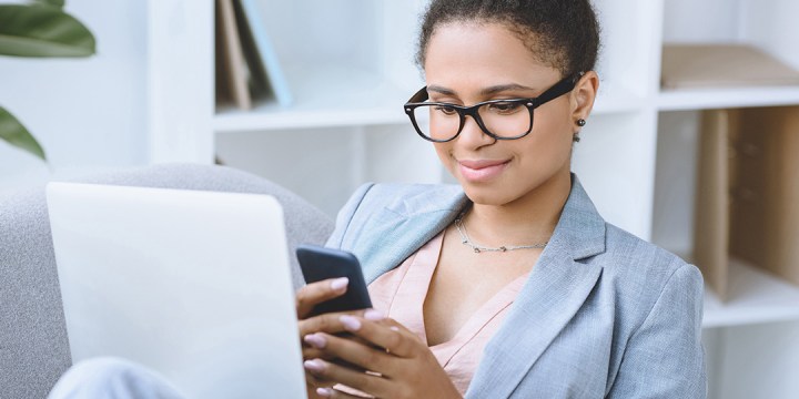 Vrouw zit ontspannen in een leunstoel, glimlacht en kijkt naar haar smartphone