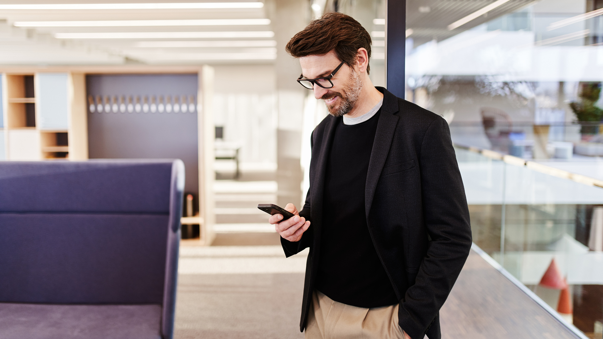 Mann blickt lächelnd auf sein Smartphone in moderner Büro-Umgebung