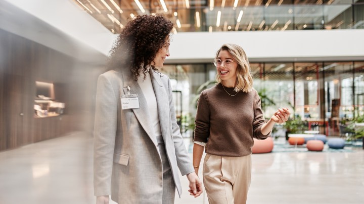 Twee vrouwen praten met een glimlach en lopen door een modern kantoorgebouw