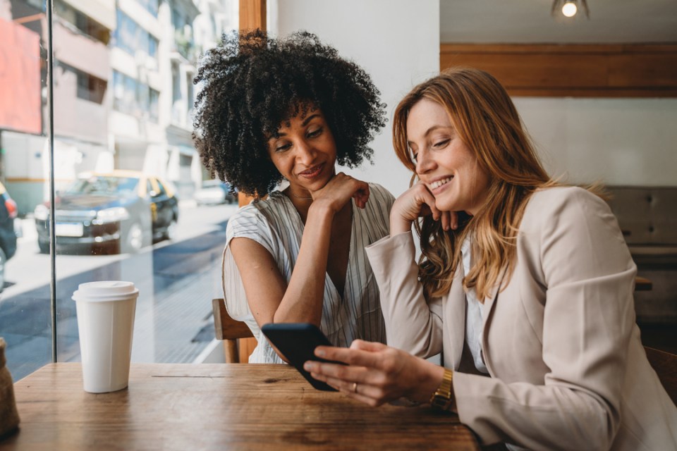 Twee vrouwen in een café kijken glimlachend naar een smartphone